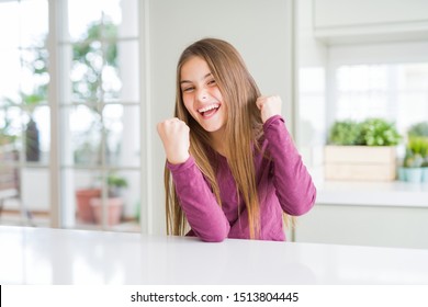 Beautiful Young Girl Kid On White Table Very Happy And Excited Doing Winner Gesture With Arms Raised, Smiling And Screaming For Success. Celebration Concept.