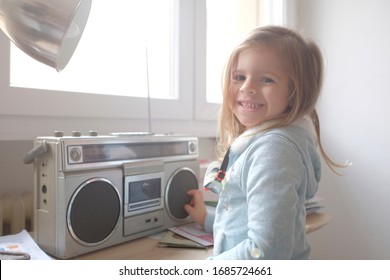 Beautiful Young Girl Kid On Wooden Table Looking Confident With Smile On Face. The Little Girl Listening Music With Vintage Stereo Player. Fun At Home. Indoor Game For Rock Girls.