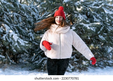 Beautiful young girl in knitted red hat runs through snowy forest. Portrait in motion - Shutterstock ID 2230770781