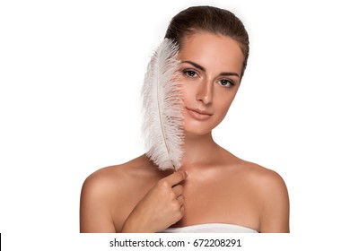 Beautiful young girl with large white feather near face. clean soft body products. Beauty Portrait. Woman Touching. Perfect Fresh Skin. Youth and Skin Care Concept. Isolated on white background