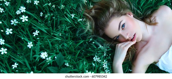 Beautiful young girl lies on a clearing among white flowers. White flowers. Chamomile. A girl with her hair in a white dress.