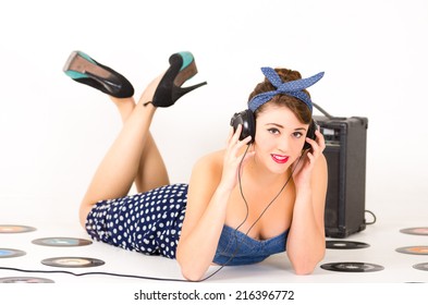 Beautiful Young Girl Listening To Headphones In Retro Clothes And Hairstyle Representing Pinup Style Lying On The Floor With Vynil Records Isolated On White