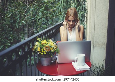 Beautiful young girl listening to music with headphones while sitting in front of an open laptop,attractive woman watching the movie on a laptop computer using headphones,home work area with computer