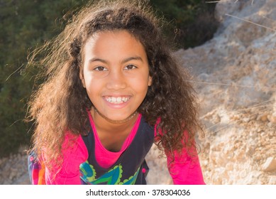 Beautiful Young Girl With Long Curly Hair Wearing A Red T-shirt.  
Portrait Of Happy Brazilian Child Playing Outside In Park With Nature Background, Pefect For Family Blogs And Magazines