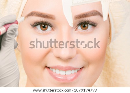 Beautiful young girl with long eyelashes tweezing her eyebrows in a beauty salon. Eyebrow Correction. Beauty Concept. Permanent Makeup. Microblading brow. Beautician Doing brows Tattooing.