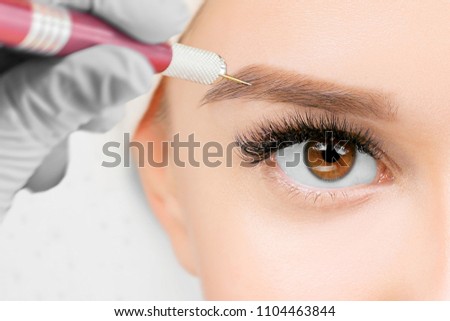 Beautiful young girl with long eyelashes tweezing her eyebrows in a beauty salon. Eyebrow Correction. Beauty Concept. Permanent Makeup. Microblading brow.  Beautician Doing brows Tattooing.