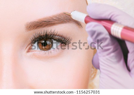 Beautiful young girl with long eyelashes tweezing her eyebrows in a beauty salon. Eyebrow Correction. Beauty Concept. Permanent Makeup. Microblading brow.  Beautician Doing brows Tattooing.