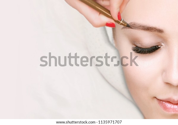 美容院で眉毛をツイーツツイーしている長いまつ毛を持つ美しい若い女の子 眉の補正 美のコンセプト パーマネントメイク マイクロブレーディング眉 眉の入れ墨をする美人 の写真素材 今すぐ編集