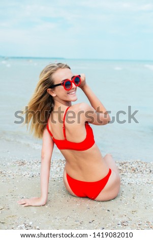 A beautiful young girl with long hair in a red swimsuit  relax on beach in the sea in sunny hot day
