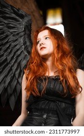 beautiful young girl with long red hair and black wings in a dark room - Shutterstock ID 2311773997