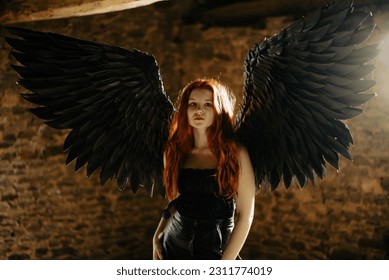 beautiful young girl with long red hair and black wings in a dark room - Shutterstock ID 2311774019