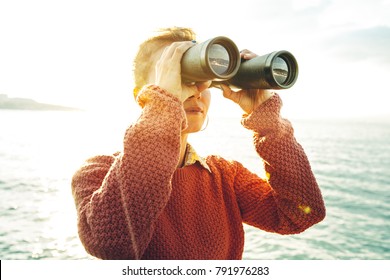 Beautiful Young Girl Looking Through Binoculars At The Sea On A Bright Sunny Day. Wanderlust Journey Concept