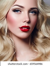 Beautiful young girl with luxurious light wavy hair close-up in the studio. Blonde - shiny, light long hair, curls. Makeup - arrows, red lipstick, pink blush. Cosmetics, hair care.