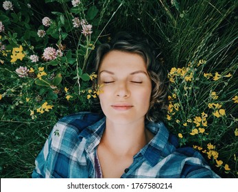 Beautiful Young Girl Lying Sleeping In Grass Among Summer Flowers Nature Outdoor. Pretty Middle Age Woman Lying Dreaming On Ground In Park. Connection Unity With Nature. 