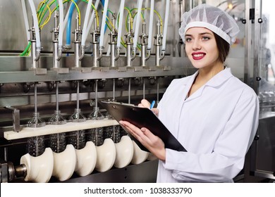 beautiful young girl is making notes on a sheet of paper on the background of a line on food production of sunflower oil.