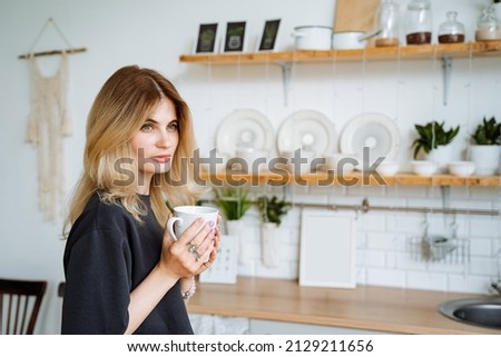 Beautiful young girl with a mug in her hands. Drink hot tea at home in the kitchen. Hold the cup in your hand to look away. Cozy interior of the dining room.