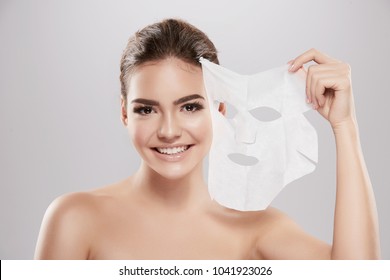 Beautiful Young Girl  With Naked Shoulders Posing At Grey Background With Facial Mask, Skin Care Concept, Beauty Photo, Skin Treatment, Spa Procedure.