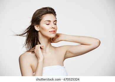 Beautiful young girl with perfect clean skin smiling touching hair over white wall. Facial treatment. Closed eyes. - Shutterstock ID 670525324