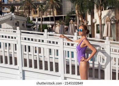 Beautiful young girl with perfect slim figure with long wet hair and bathing suit in fashionable stylish sun glasses sitting on the steps of swimming pool swim, sunbathe, have fun at beach party