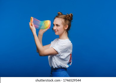 Beautiful young girl playing with a rainbow slinky, a toy of her childhood on a blue background