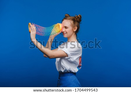 Beautiful young girl playing with a rainbow slinky, a toy of her childhood on a blue background