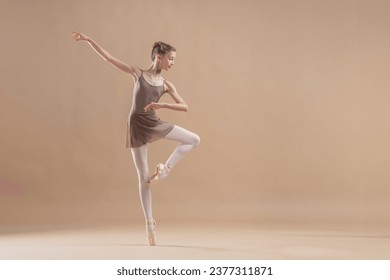 Beautiful young girl professional student ballerina in pointe shoes and a leotard on light beige background. - Powered by Shutterstock