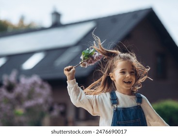 Beautiful young girl with purple lilacs flower in hands. Young girl spending time outdoors in nature, springtime. House with solar panels in background. - Powered by Shutterstock