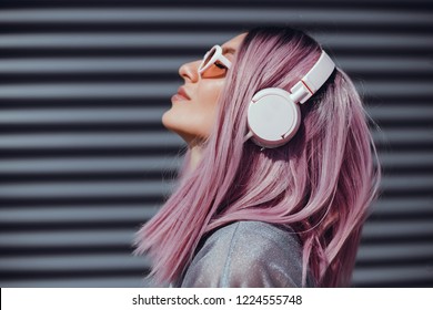 Beautiful young girl with purple pink hair listening to music on headphones, street style, outdoor portrait, hipster girl, music, mp3, Bali, beauty woman, sunglasses, orange color, concept