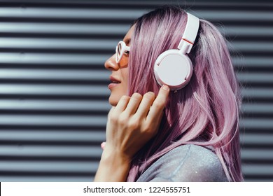 Beautiful young girl with purple pink hair listening to music on headphones, street style, outdoor portrait, hipster girl, music, mp3, Bali, beauty woman, sunglasses, orange color, concept - Shutterstock ID 1224555751