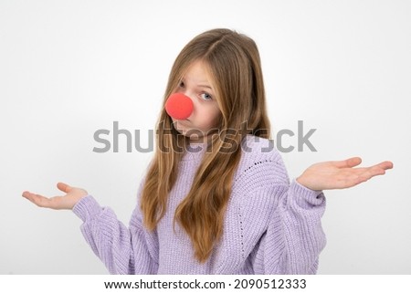 beautiful young girl with red clown nose posing in front of white background and is wearing a purple wool sweater 