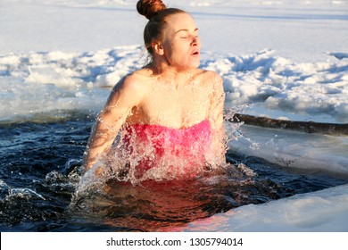 A beautiful young girl, with red hair, a side-piece swimsuit, dives into the icy water in the winter on the lake on a beautiful sunny day. Ukraine, Sumy Oblast, Shostka