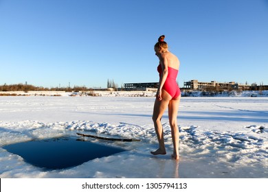 A beautiful young girl, with red hair, a pink swimsuit, getting ready to dive into the icy water in the winter on the lake on a beautiful sunny day. Ukraine, Sumy Oblast, Shostka
