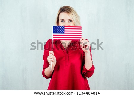 beautiful young girl in a red shirt on a white background holds a small flag of America in her hand