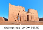 A beautiful young girl in shorts is standing watching and historical artifacts - Ancient Egyptian relics in the Temple of Horus - Edfu, Egypt.