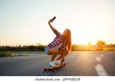 Beautiful young girl sits on longboard in sunny weather.