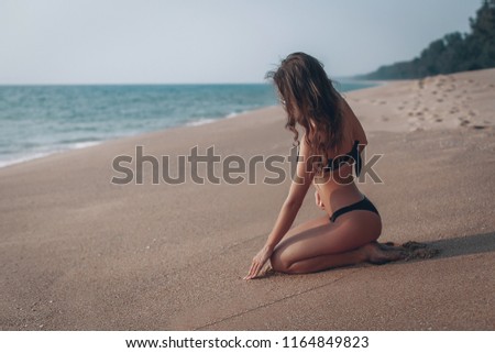 Beautiful young girl sitting back on the sand and looking at the sea