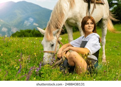 Beautiful young girl sitting next to her white horse at sunset in the mountains on the flower field - Powered by Shutterstock