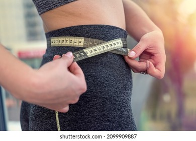 beautiful young girl with a slim waist and a flat stomach measures the waist circumference with a measuring tape. The concept of centimeters of the body. Diet and sport concept.