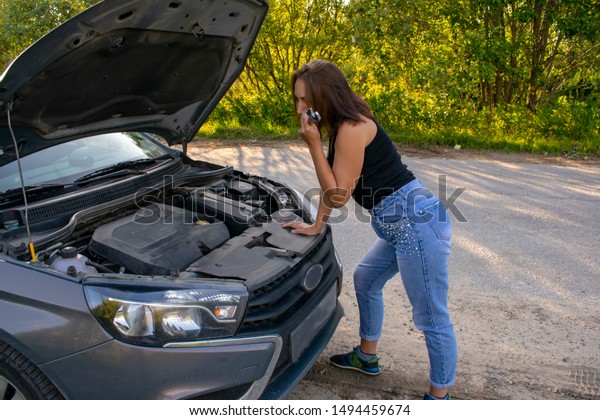 A beautiful\
young girl stands in front of the car with the hood open and does\
not know what broke down in the\
car.