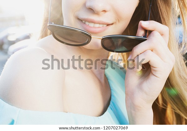 Beautiful young girl with sunglasses\
smiling on sunny street. Anonymous lifestyle\
Concept