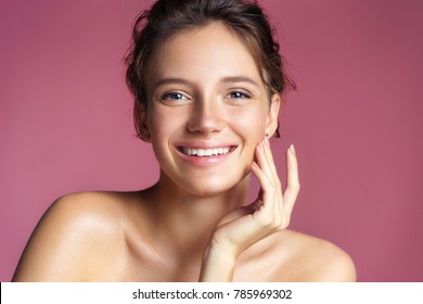 Beautiful young girl touching her perfect skin on pink background. Skin care concept
