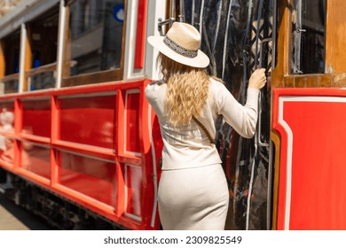 Beautiful young girl tourist in a hat poses in front of tram at popular Istiklal street in Beyoglu, Istanbul, Turkey 