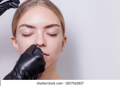 Beautiful Young Girl Tweezing Her Brows In A Beauty Salon. Beauty Concept. Cosmetologist Plucks Client Eyebrows By Thread. Eyebrow Correction, Threading. Permanent Makeup. Microblading Brow. Close Up.