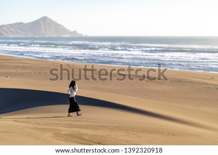 Beautiful young girl walking along the beach sand dunes step by step letting it footprints in the sand. An amazing wild beach during a sunny day at sunset time in Topocalma Beach, an awe coast scenery