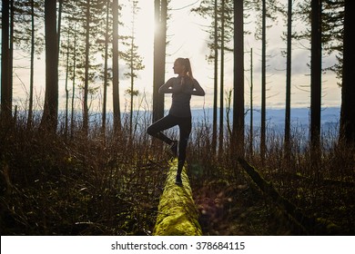beautiful young girl walking in forest standing on log in yoga tree pose