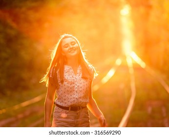 Beautiful young girl walking on the tram rail in the sunset rays on the summer park alley.