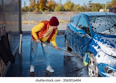 Beautiful young girl washes the car at the self-service car wash. erasing dirt to the car with a brush