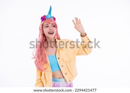 Beautiful young girl waving at someone while shooting process showing different emotions in unicorn funny headband and pink wig in white studio isolated.