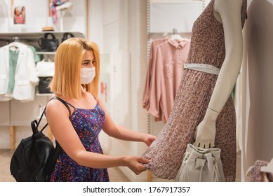 Schönes junges Mädchen mit Einweg-Gesichtsmaske wählt Kleidung im Kleiderladen.Leben mit neuen Normalzustand während covid19 Ausbruch.