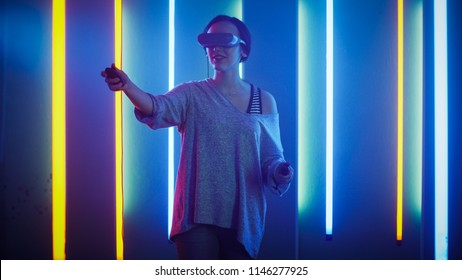 Beautiful Young Girl Wearing Virtual Reality Headset Using Joysticks / Controllers. Creative Young Girl Does Concept Art With Augmented Reality. Playing Online Video Game. Neon Retro Lights Surround.